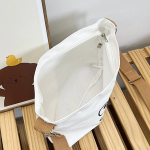 Top view of white canvas crossbody bag interior showing zip pocket and metal buckle