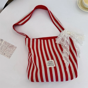Detail of red striped canvas bag featuring lace bow and logo label on white table