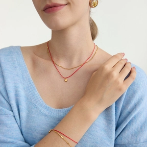 Détail d'un collier double épaisseur avec pendentif cœur et bracelet en cordon rouge