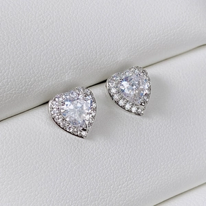 Macro detail of heart-shaped zircon stud earrings with a halo setting in a white jewelry box