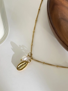 Detailed shot of golden shell pendant with pearl on delicate stainless steel bead chain