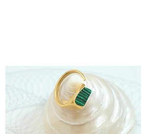 Dettaglio macro del polsino placcato oro 18k con pietra verde su una conchiglia