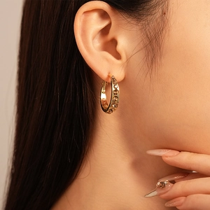Close-up of golden geometric hoop earring with champagne crystals worn by model