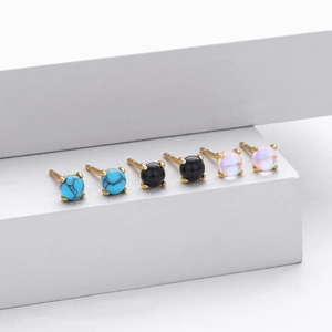 Close-up of three pairs of stud earrings with turquoise, black, and opal stones in gold claws