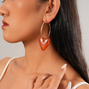 Close-up of model wearing gold hoop earrings with amber acrylic heart pendants