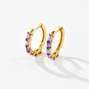 Detalle de pendientes de aro dorados con cinco piedras moradas con corte baguette
