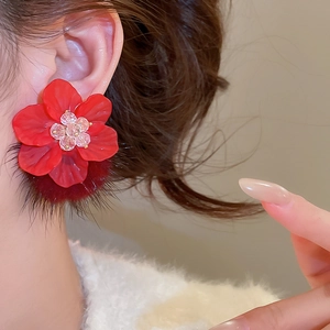 Detailed close-up of a red acrylic flower earring with a plush pom-pom back detail