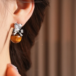 Macro view of zircon heart and brown tiger eye bead earring on a model ear
