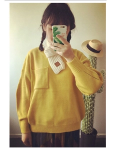 Detail of soft white knitted scarf with small brown label on a yellow knit sweater