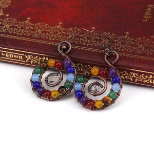 Detail of handmade bronze spiral earrings with colorful chakra healing stones on a book