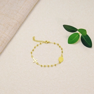 Detail of gold beaded bracelet with a cross charm and religious medal on a soft surface
