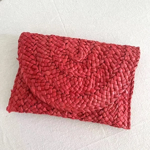Flat lay of red handmade woven straw clutch bag on a white textured fabric background