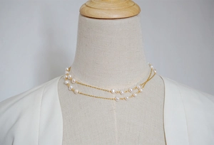 Detailed view of a double-layered gold chain necklace with white freshwater pearls
