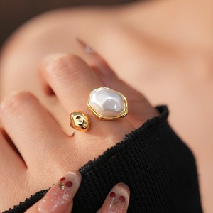 Détail d'une bague irrégulière dorée avec perle baroque blanche portée au doigt du modèle
