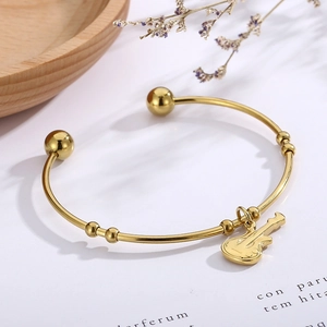 Detail view of a gold violin-themed open bangle with musical instrument charms