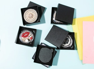 Macro view of crystal and pearl compact mirrors displayed in a black gift box packaging