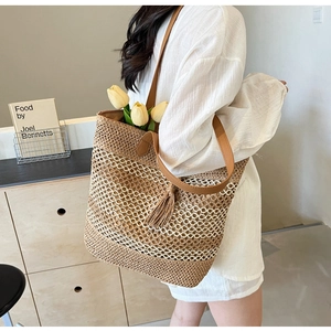 Detail of woven straw tote bag with brown leather straps and a stylish decorative tassel