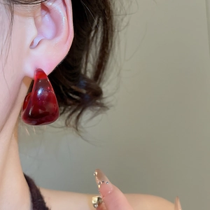 Close-up of deep red resin C-shaped earrings with translucent gemstone texture and gloss