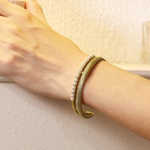 Detail of a gold double-layer bracelet with white pearls and snake bone texture on wrist