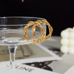 Macro detail of gold twisted hoop earrings hanging on a glass rim with sharp metal texture