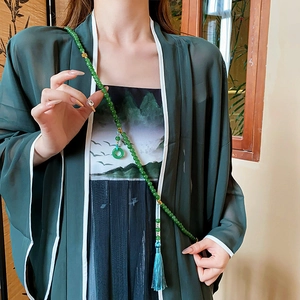 Détail du collier de perles vertes avec pendentif boucle et pompon en soie bleue