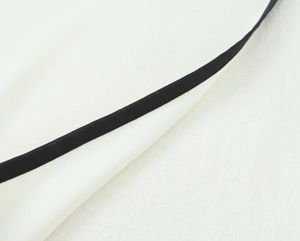 Detailed close-up of white crepe fabric with contrast black trim and stitching