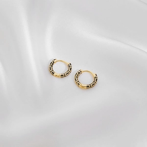 Close-up of gold hoop earrings with black enamel geometric pattern on white silk fabric