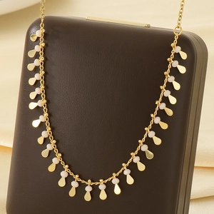 Detail view of a gold collarbone chain with oval pendants and white beads on a black stand
