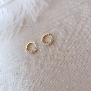 Detail of gold hoop earrings with small white pearls on elegant linen with white feather