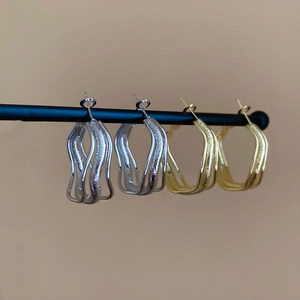 Detailed view of irregular twisted gold and silver metal hoop earrings on a black display bar