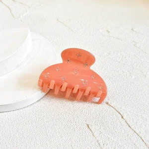 Detail of coral pink rhinestone hair claw clip with star glitter on white marble surface