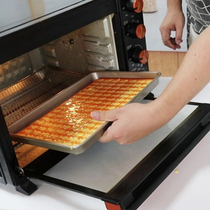 Placing rectangular baking tray with small fish snacks into a kitchen oven