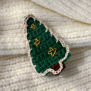 Macro view of hand-knitted green Christmas tree hair clip with golden stars detail