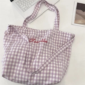 Detailed shot of purple plaid tote bag with red embroidered script on white surface