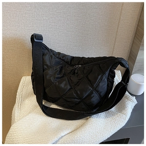 Close-up of black quilted nylon dumpling bag with adjustable fabric strap on soft fabric