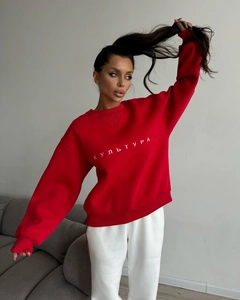 Detail of red crewneck sweatshirt featuring white Cyrillic embroidery and soft fabric texture