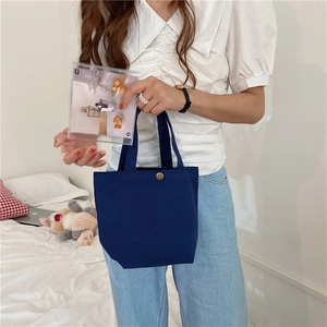 Detail of navy blue canvas lunch bag with gold metal button held by a model