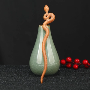 Detail of hand-carved snake-shaped sandalwood hair stick in a green ceramic vase