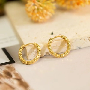 Golden circle earrings with textured diamond-cut design on minimalist stone stand