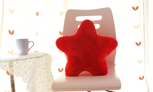 Red star-shaped plush pillow placed on a modern white chair in a bright indoor setting
