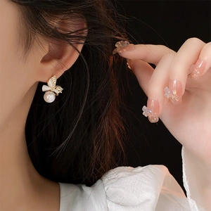 Close-up of elegant gold bow earrings with white pearl drop on female model