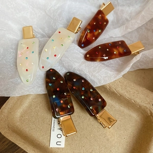 Detailed view of six acrylic hair clips with rhinestones in cream and tortoise patterns