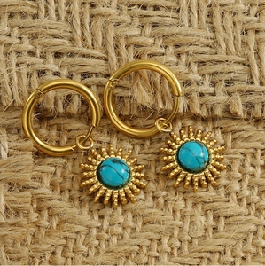 Close-up of 18K gold-plated sunflower earrings with turquoise stone on jute texture