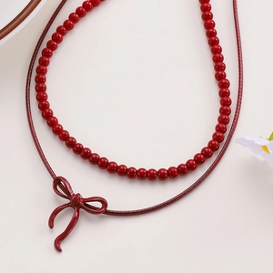 Close-up of red beaded necklace with bow pendant on a minimalist cream background