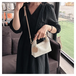 Detail of cream white pleated texture handbag with metal chain tag and adjustable strap
