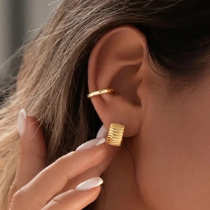 Close-up of gold ear cuff and textured wide hoop earring set worn by a female model