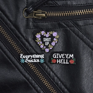 Détail de broches émaillées florales avec slogans impertinents sur une veste en cuir