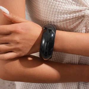Close-up of a wide black resin bangle bracelet with glossy finish on a woman's wrist
