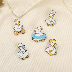 Close-up of five cute enamel duck badges with bicycle and doctor themes on fabric