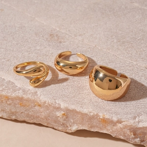 Detailed view of three polished gold geometric drop rings on a natural stone surface